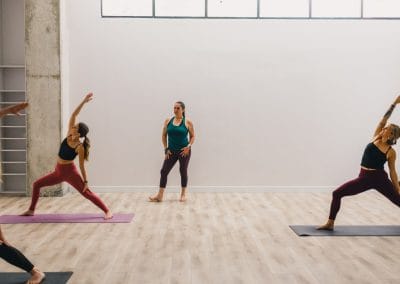 michelle young in green top and purple bottoms teaches reversed warrior to 3 yogis on mats at my vinyasa practice in austin texas