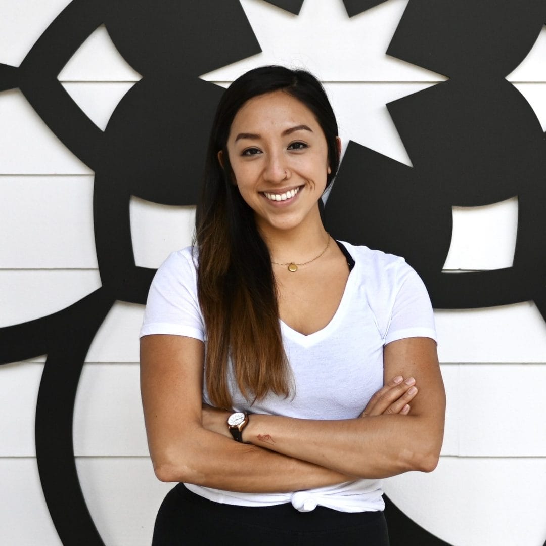 Kristiana Vuong Kristiana Vuong standing smiling wearing white top and black bottoms with arms crossed in front of the mandala at my vinyasa practice in austin texas