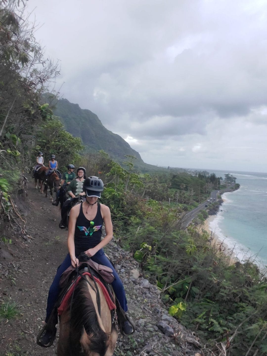 5 women yogis on horseback riding on a mountain trail overlooking the coast of the big island of Hawaii under an overcast sky of light grey clouds