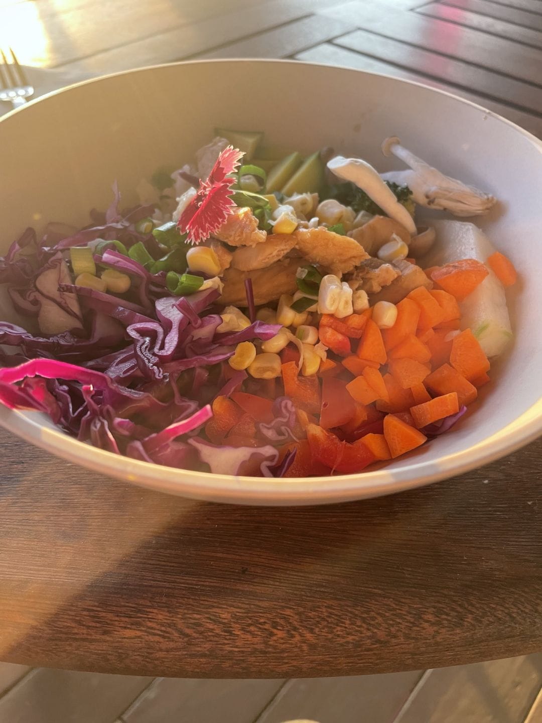 an earthen bowl of carrots, cabbage, corn, mushrooms, brussels sprouts on a wooden table
