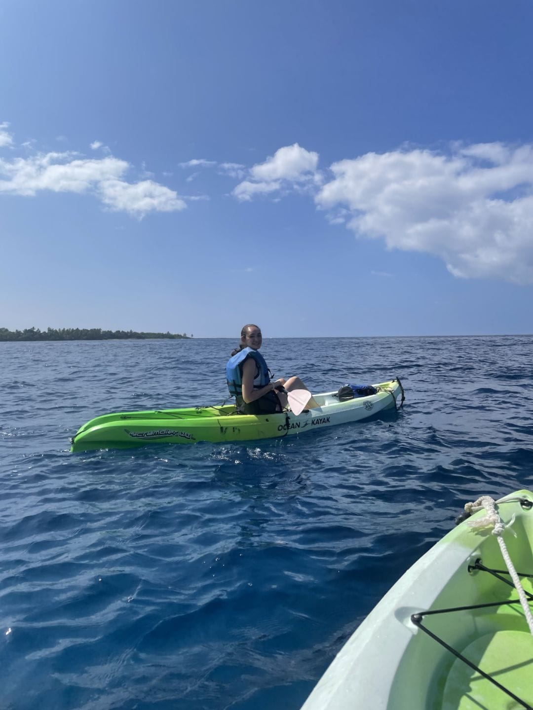 a woman yogi in a green and white one person paddle board on the ocean in Hawaii under a sunny blue sky with white clouds