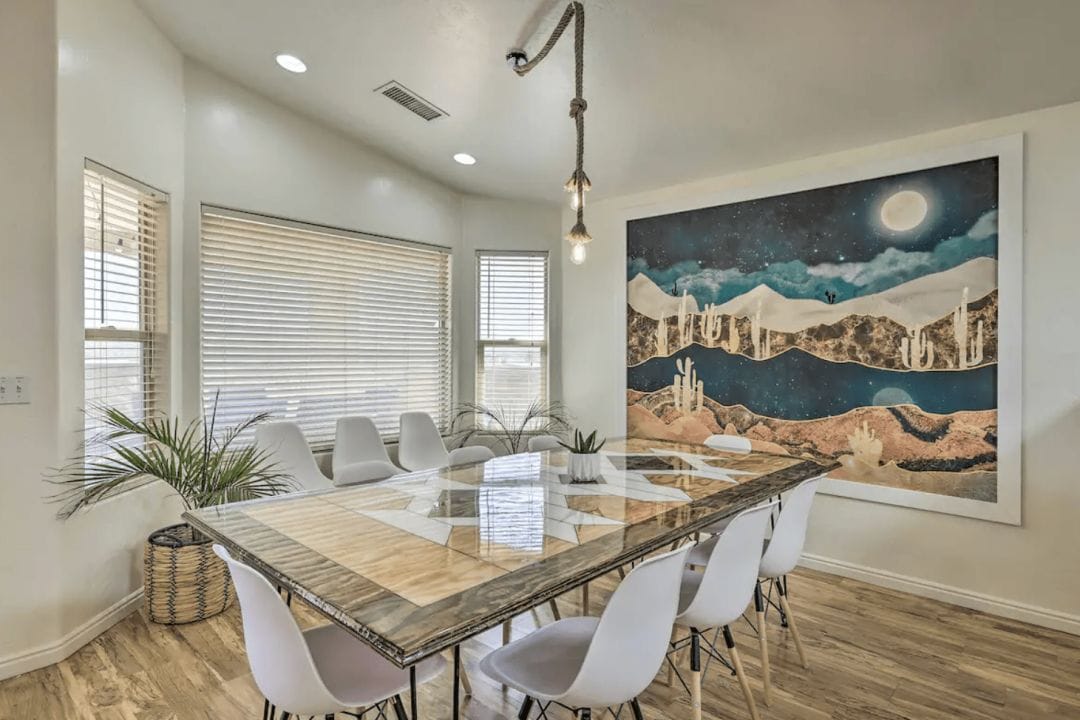 interior of a dining room in Arizona with a rectangular wooden table with 8 white chairs and a large desert painting on the wall