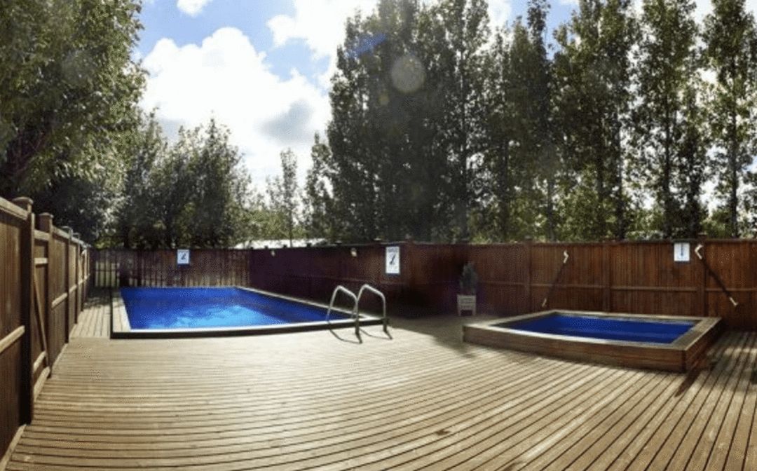 Two outdoor pools on a large wooden deck surrounded by trees on a sunny day