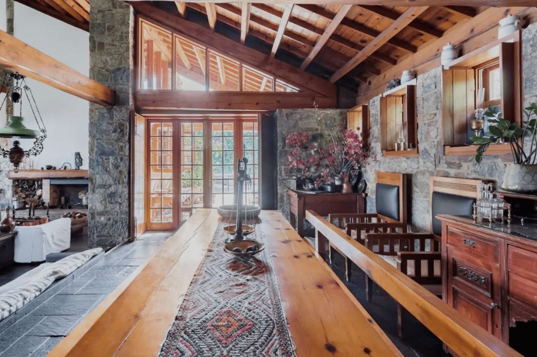 interior of a house kitchen in Greece with a long wooden table large stone-faced columns, dark stone floors and high wood ceilings