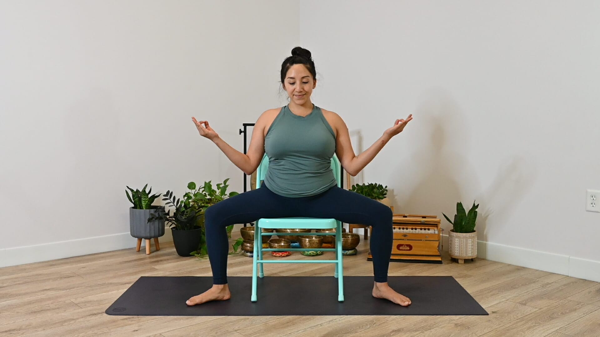 My Vinyasa Practice Adaptive Yoga Certification Hispanic woman practicing in seated goddess pose on a turquoise folding chair.