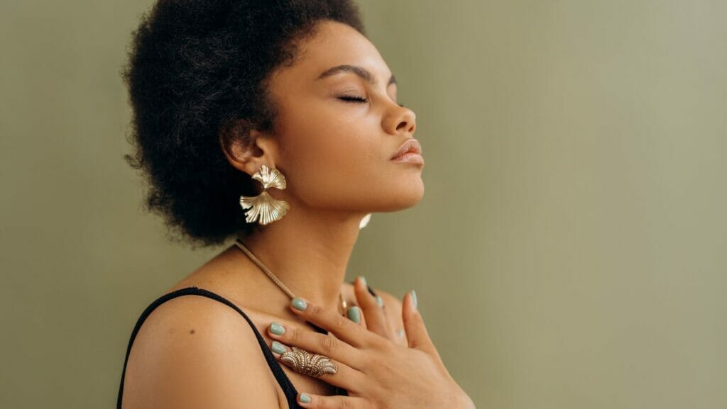 A woman with black hair stands with her eyes closed and her palms crossed over her chest.