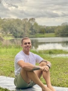 Student Alan Torres sits in front of a pond with his arms around his knees.