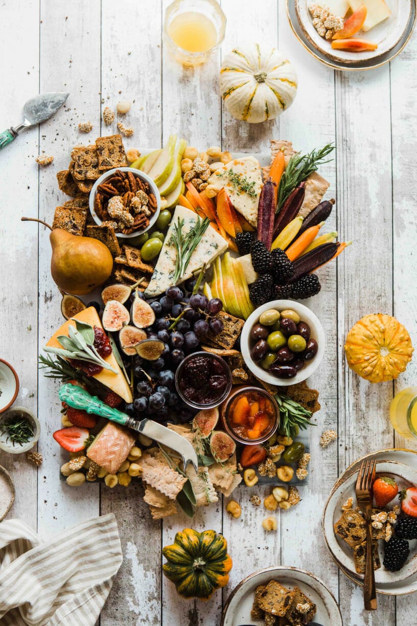 An image of a wooden board full of food. There are fruits, cheeses, bread, and spreads.