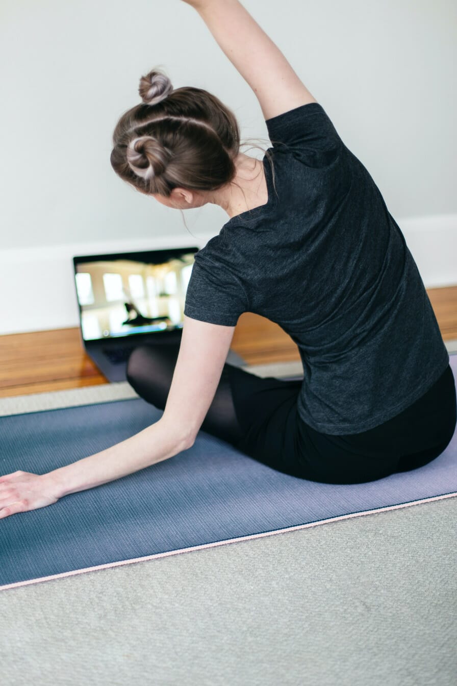 A woman sitting on a yoga mat, following along to a yoga class