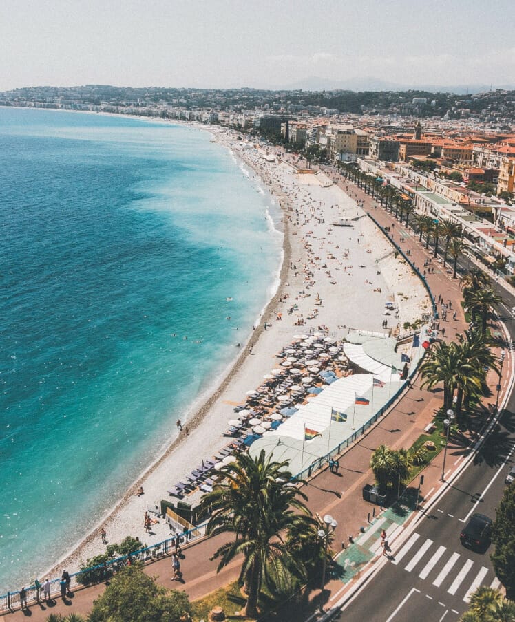 A photo of the beach in Nice, France. There is water and sand visible, with buildings along the coast.