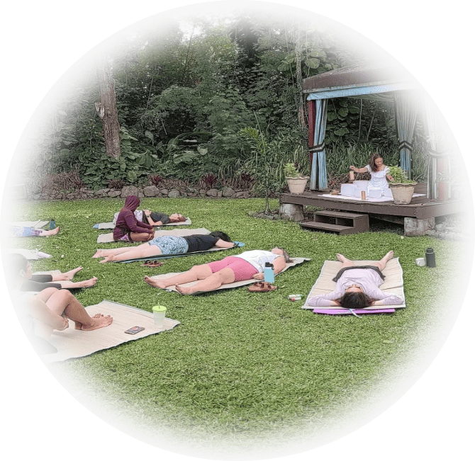 A group of yogis laying on the grass in yoga mats.