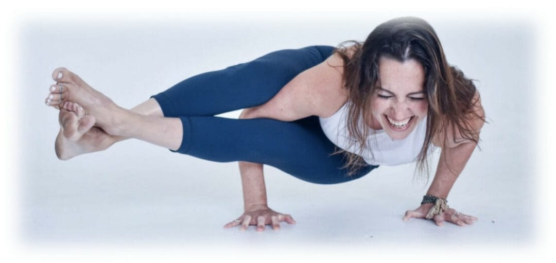 Michelle Young, the founder of MVP is in a white yoga studio. She is balancing on her hands with both legs in the air, horizontally to her right side. She has a large smile and is laughing.